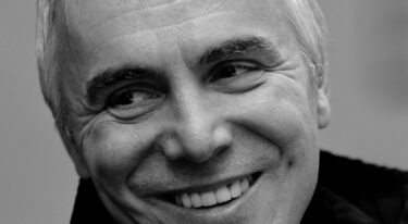 Črno-beli portret nasmejanega moškega od blizu.