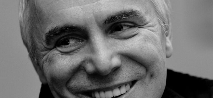 Črno-beli portret nasmejanega moškega od blizu.