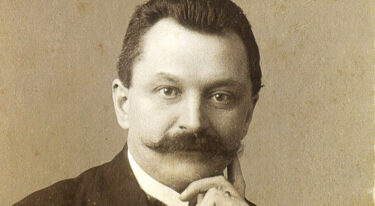 Črno-beli portret moškega z brki v obleki; roka je prislonjena k obrazu.